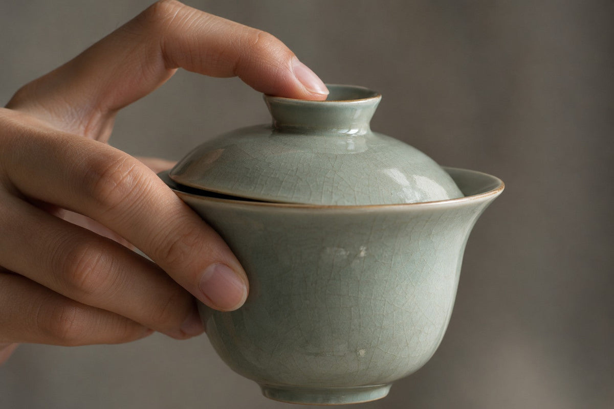 Close view of a hand holding a celadon gaiwan and its lid