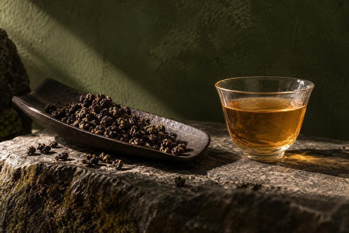 Rolled oolong leaves in a dark tea scoop beside a golden infusion